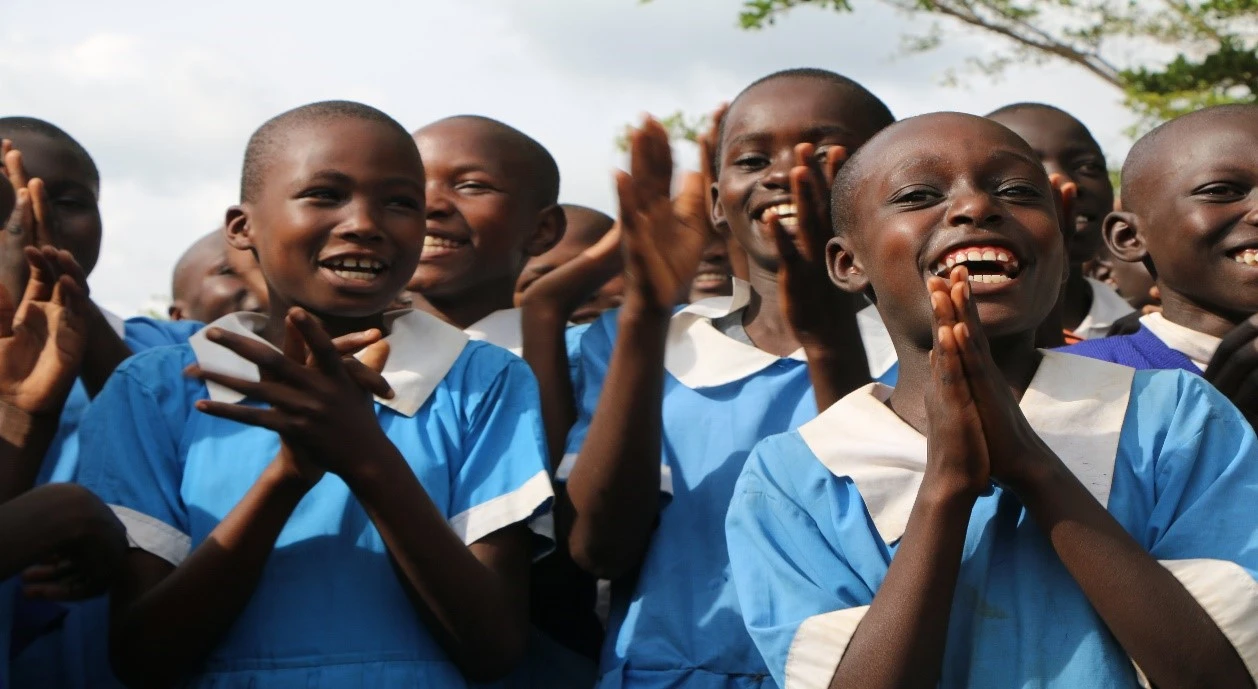 Happy children clapping at a school in Tanzania, where a Save the Children project, focused on education for peacebuilding, has improved sanitation and menstrual hygiene management.