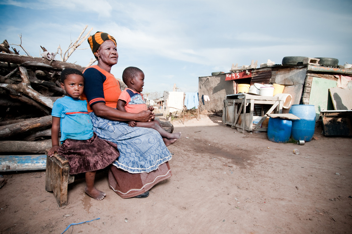 Poor African family, grandmother with baby boy and little girl sitting outside their hut.