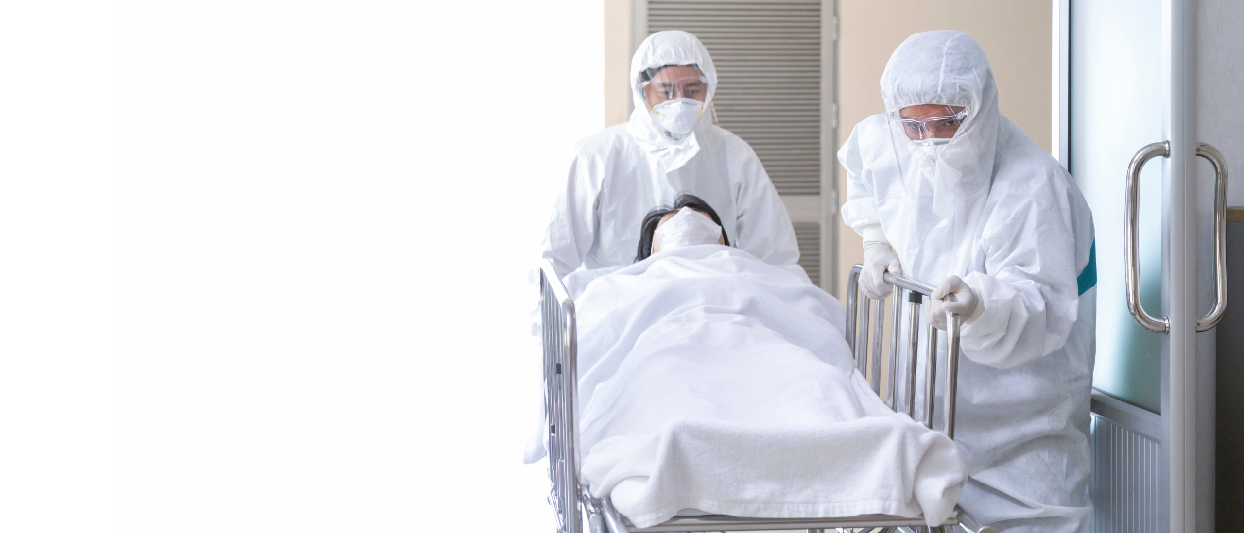 Nurse and doctor in full PPE suits and face masks pushing a seriously ill patient on a gurney towards a quarantine room, illustrating protocols for protecting healthcare workers Ebola Uganda.