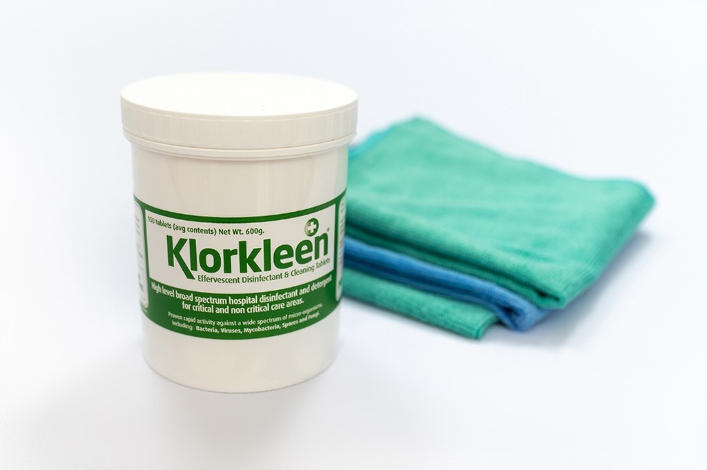 Klorkleen broad spectrum disinfectant tablets in a white container next to folded green cloths, effective against a range of pathogens.